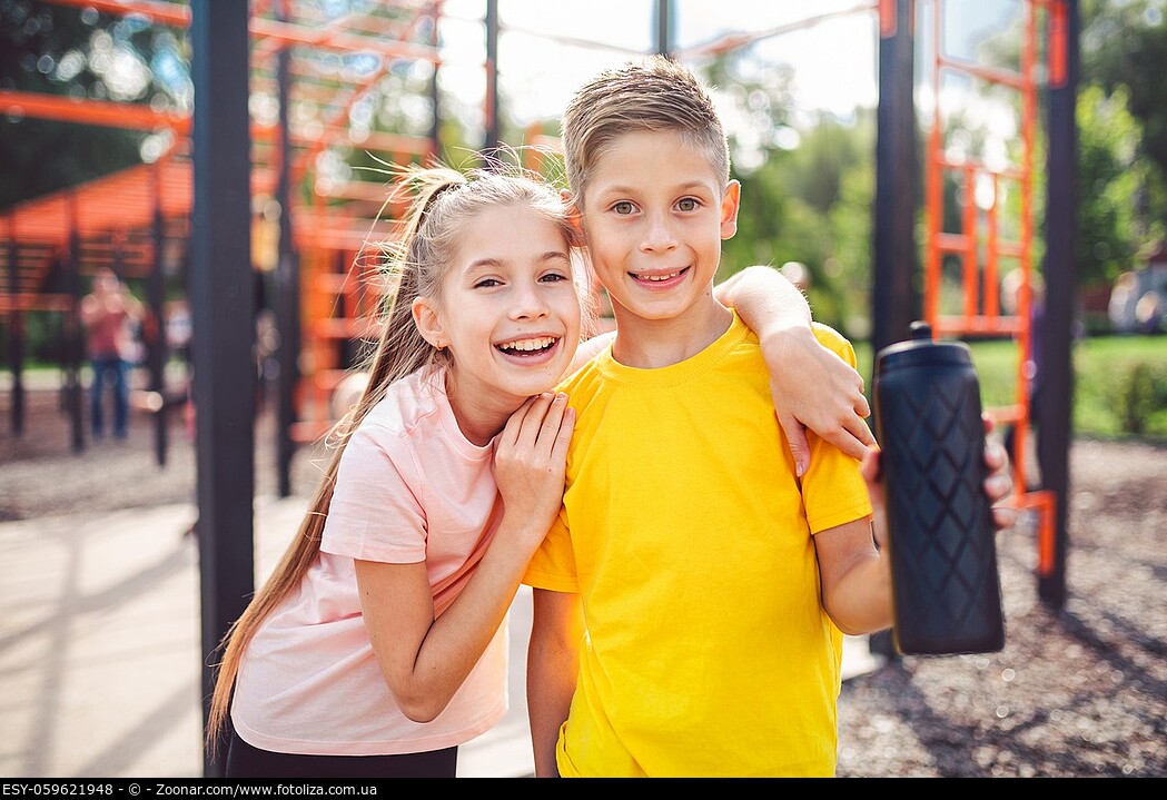 Teens children and sports theme. Two kids athletes twins rest and replenish their thirst during workout outdoor gym workout in sunny summer weather. S...