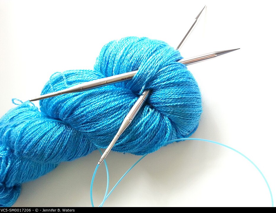 Close-up of yarn and knitting needles on a white background.