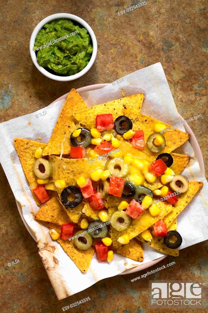 Stock Photo: Baked nachos with cheese, green and black olives, red bell pepper and corn, with guacamole on the side, photographed overhead on slate with natural light.