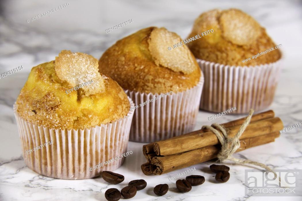 Stock Photo: three delicious cupcakes, coffee grains and cinnamon sticks on marble background.
