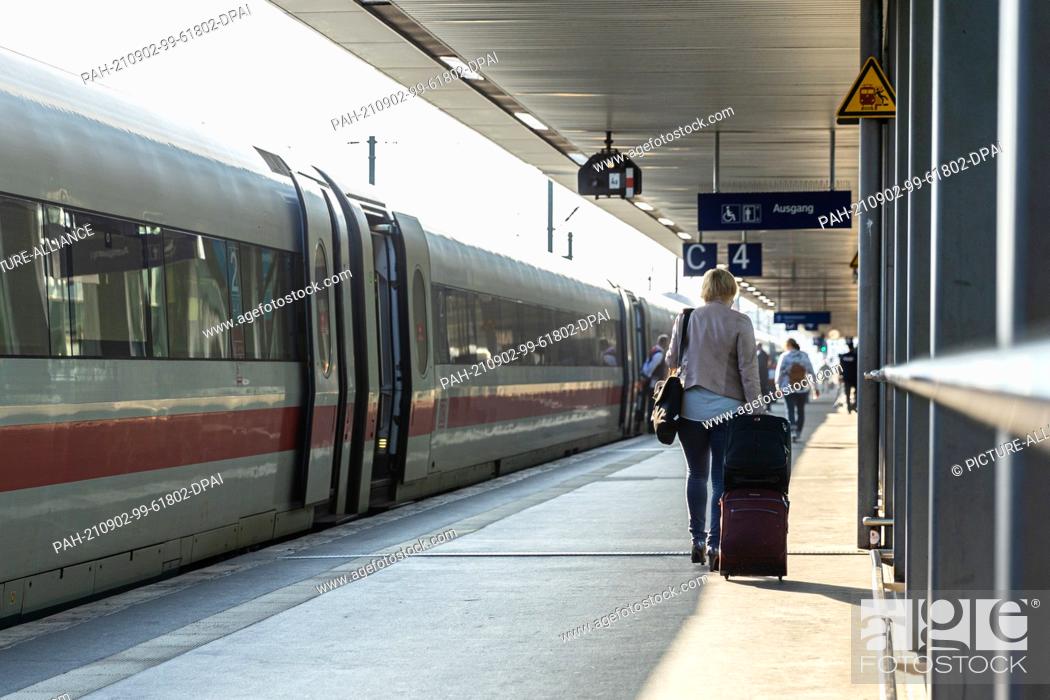 Stock Photo: 02 September 2021, Lower Saxony, Hanover: A woman walks along a platform with a suitcase in Hanover central station. There is an ICE train on the track.
