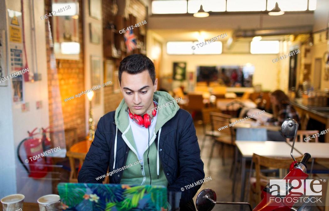 Stock Photo: Focused young male college student studying at laptop in cafe window.
