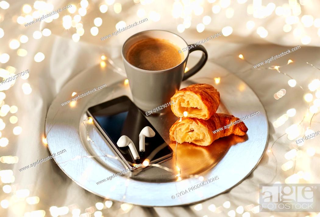 Stock Photo: smartphone, earphones, coffee and croissant in bed.