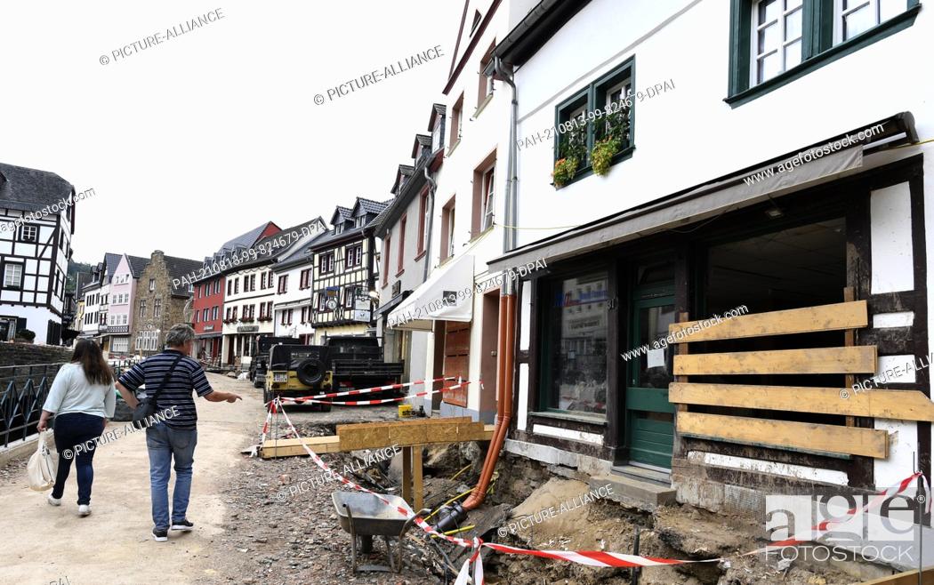 Stock Photo: 12 August 2021, North Rhine-Westphalia, Bad Münstereifel: Passers-by walk along a street in the Eifel village where reconstruction has begun a month after the.