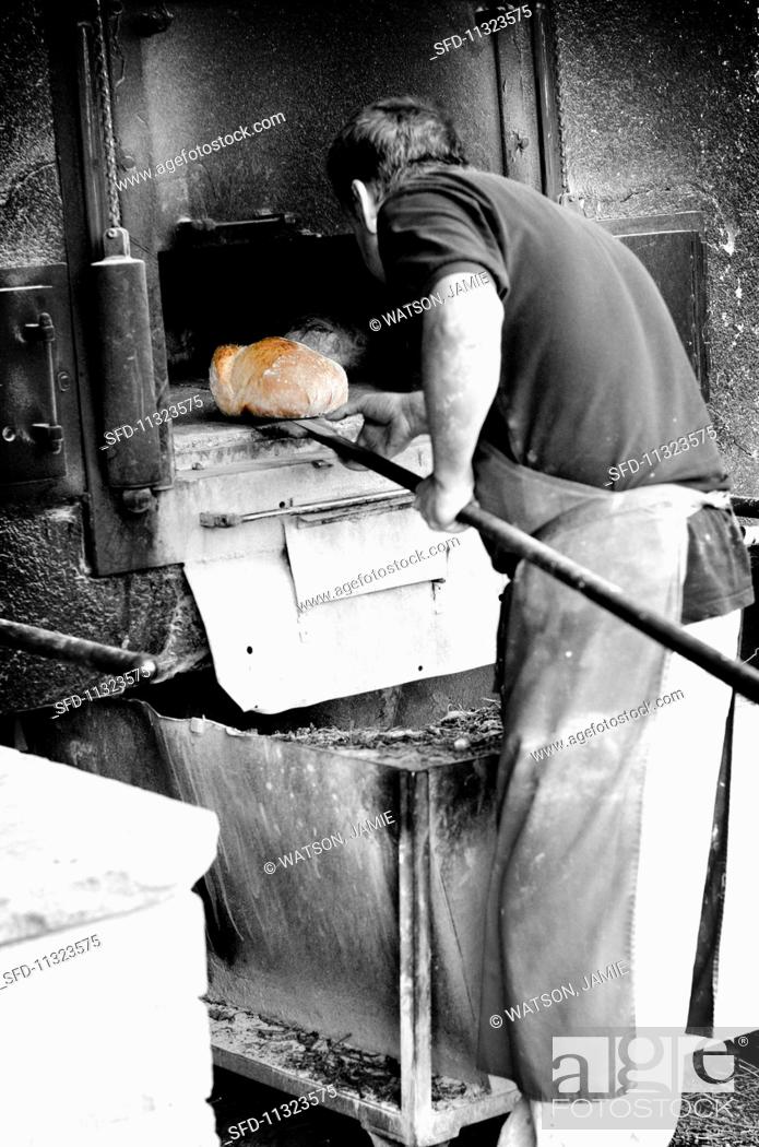 Stock Photo: A baker removing a golden brown loaf from the oven.