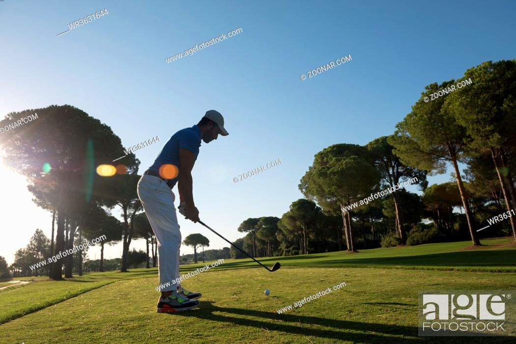 Photo de stock: golf player hitting shot with club on course at beautiful morning with sun flare in background.