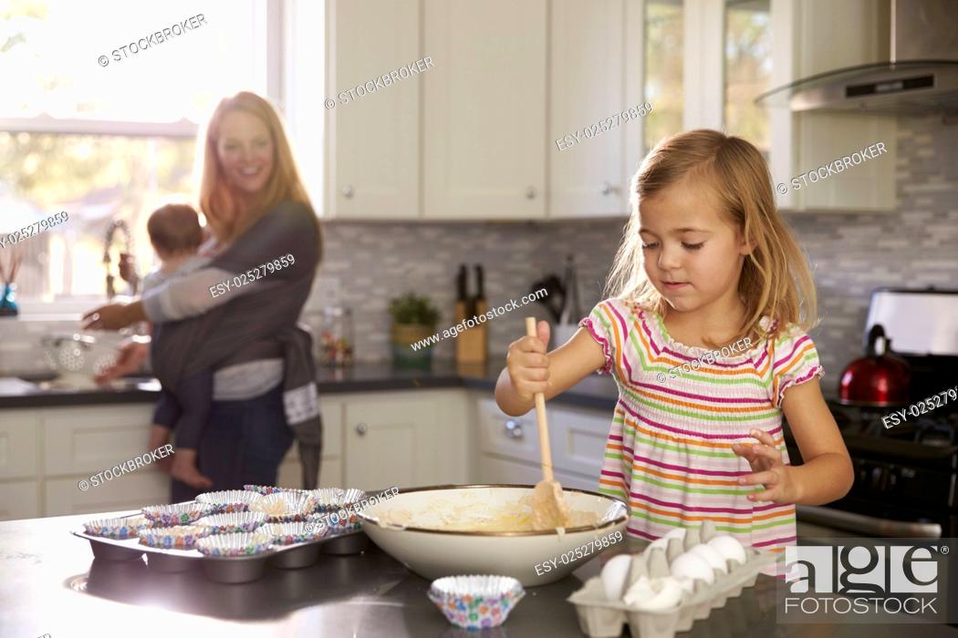 Stock Photo: Young girl prepares cake mix, mum and baby in the background.