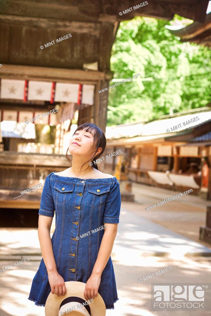 Stock Photo: Young woman wearing blue dress and holding hat at Shinto Sakurai Shrine, Fukuoka, Japan.
