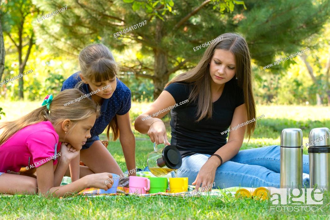 Stock Photo: Family on a picnic, girl pours tea in glasses, children watch.