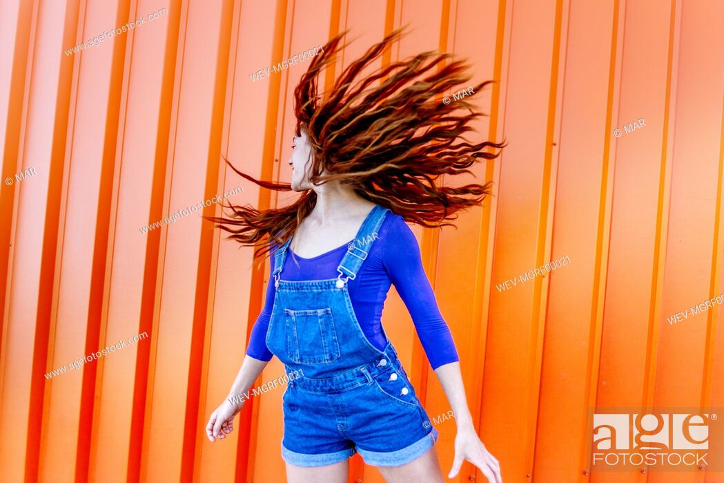Stock Photo: Playful woman tossing hair while standing against orange wall.