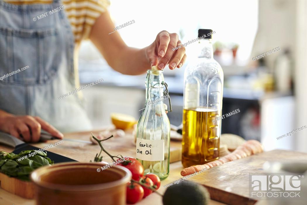 Stock Photo: Woman putting garlic into bottle of olive oil in kitchen.