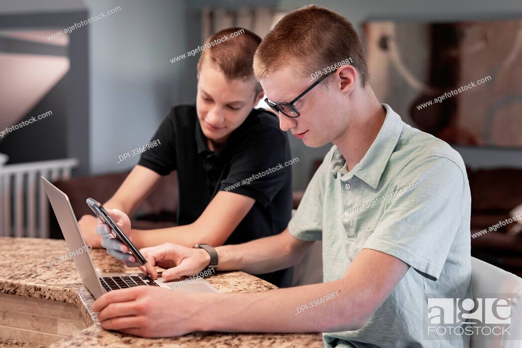 Stock Photo: Young adult brothers using laptop computer and smart phone together at home; Edmonton, Alberta, Canada.