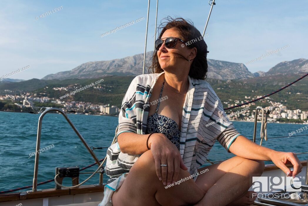 Stock Photo: A woman sits on the deck of a sailboat with windswept hair looking out along the coast of Montenegro; Montenegro.