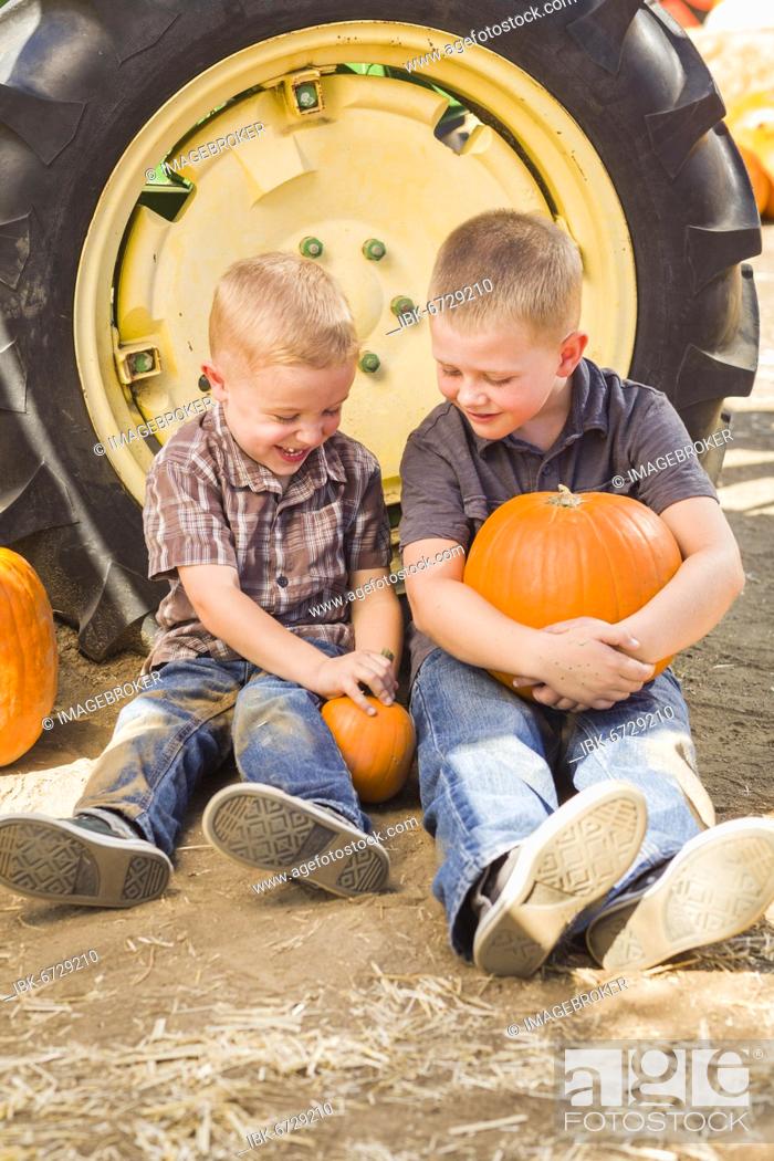 Stock Photo: Two boys sitting against a tractor tire holding pumpkins and talking in rustic setting.