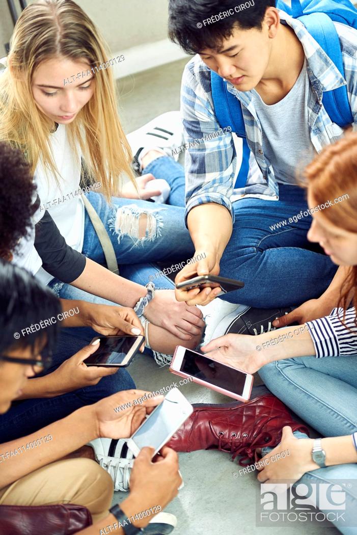 Stock Photo: Group of students sitting together on floor, looking at smartphones.