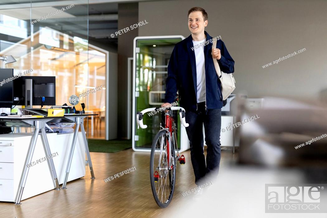 Stock Photo: Smiling businessman with bag and bicycle walking while leaving after work from office.