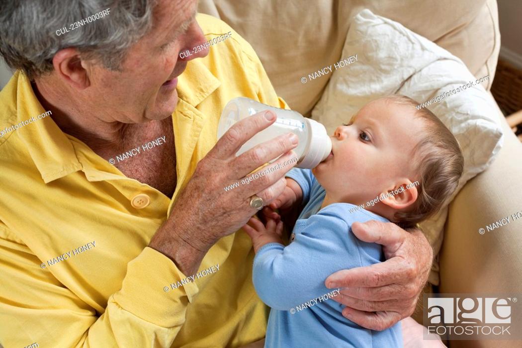 Stock Photo: Grandad feeding grandson milk bottle.