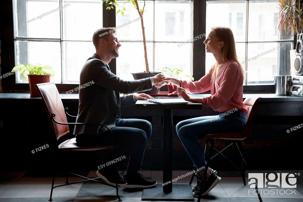 Stock Photo: Female HR manager and male applicant shake hands greeting each other start job interview sit in cafe table. Client and services representative accomplish.