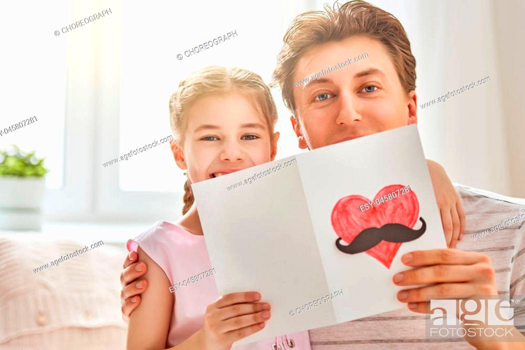 Stock Photo: Happy father's day! Child daughter congratulates dad and gives him postcard. Daddy and girl smiling and hugging. Family holiday and togetherness.