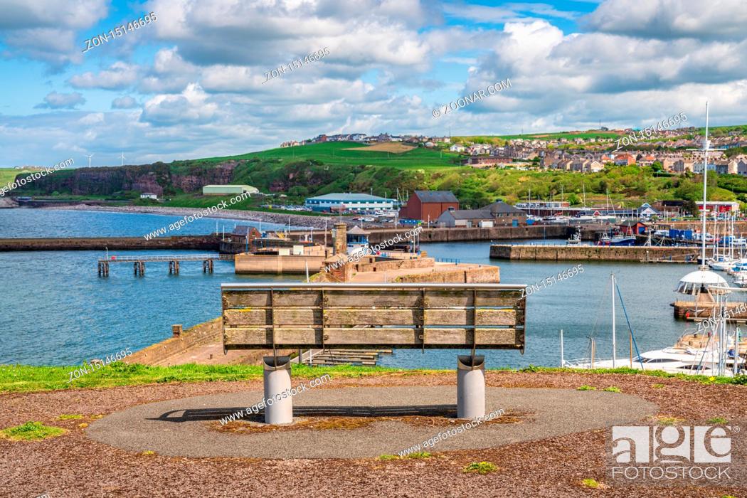 Stock Photo: Whitehaven, Cumbria, England, UK - May 03, 2019: A bench with a view over the Whitehaven Marina and Bransty in the background.