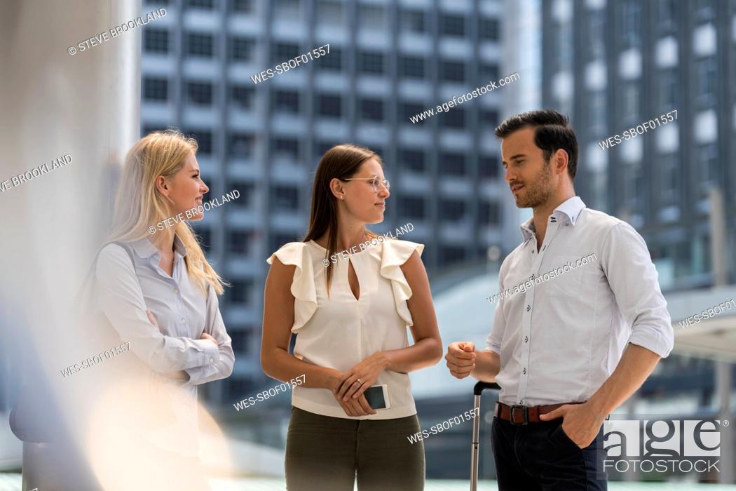Stock Photo: Smiling business colleagues talking in the city in front of skyscraper.