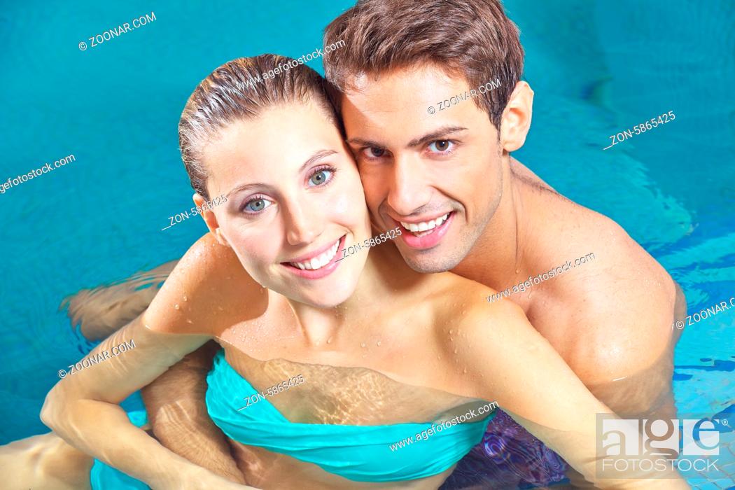 Stock Photo: Zufriedenes Paar sitzt lächelnd zusammen im Wasser vom Pool eines Hotels.