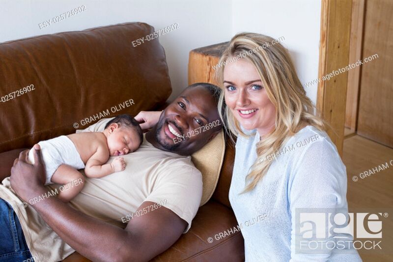 Stock Photo: A mother and father with their newborn baby daughter at home. They are looking at the camera and smiling.