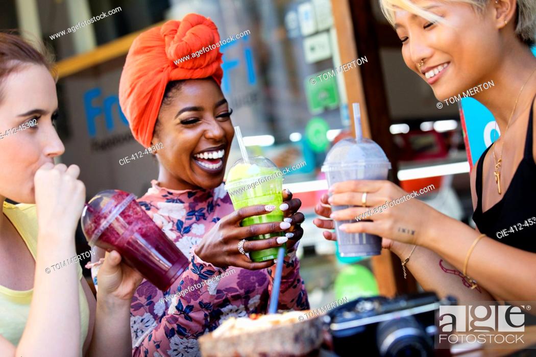 Photo de stock: Young women friends drinking smoothies at sidewalk cafe.
