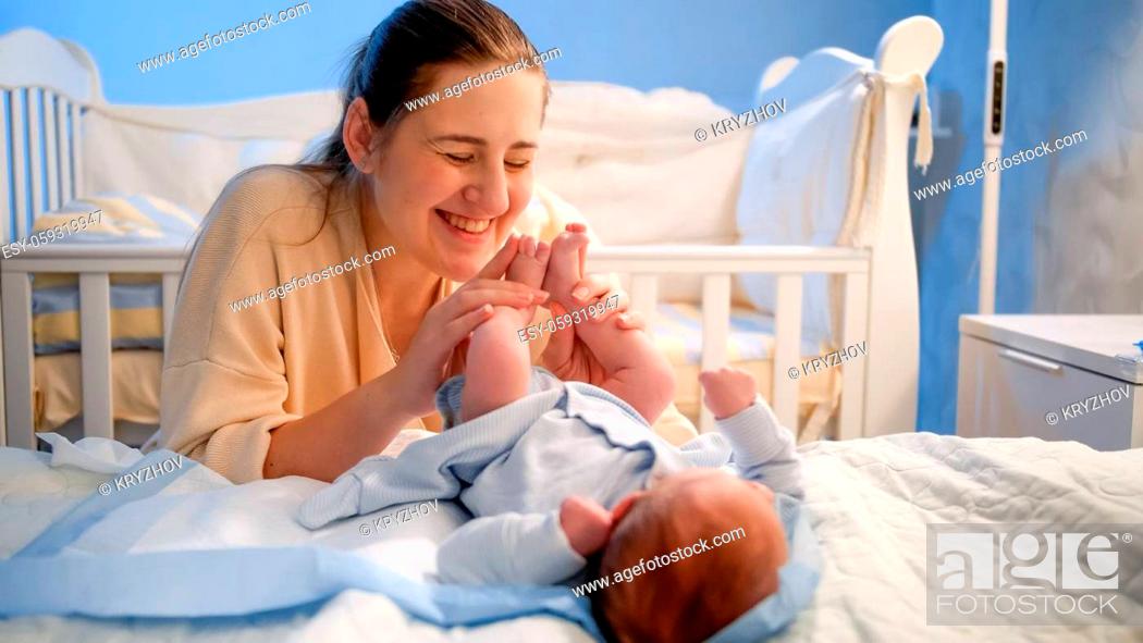 Stock Photo: Happy smiling young mother looking at her newborn baby sleeping in bed at night.
