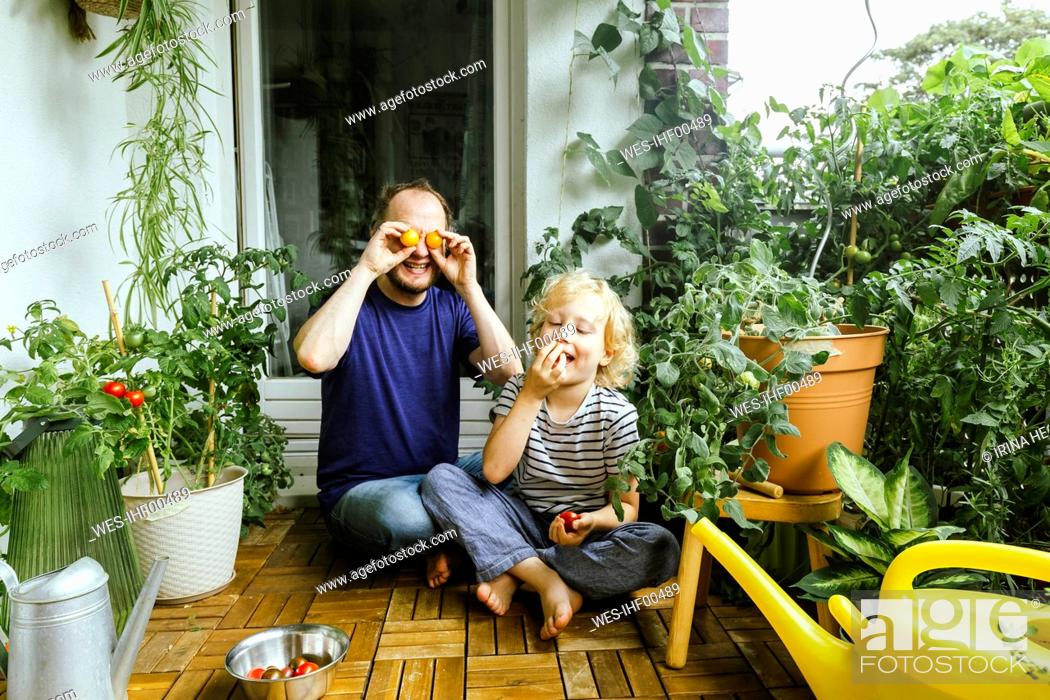 Stock Photo: Smiling father covering eyes with tomatoes while sitting with son in balcony.