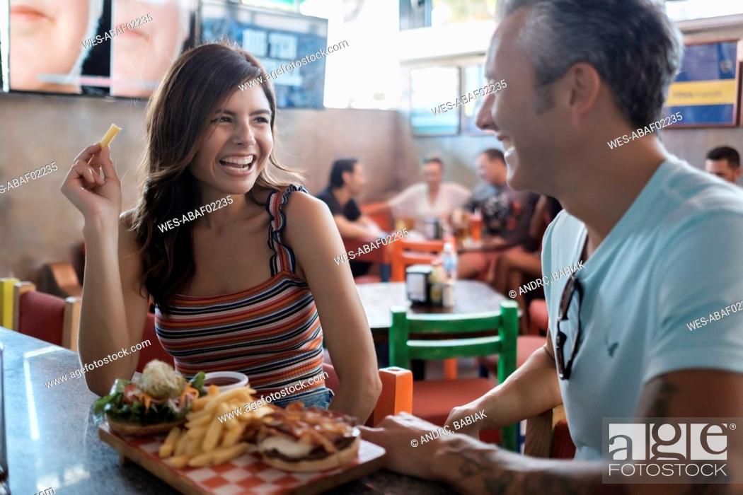 Stock Photo: Happy couple sharing hamburger and French fries in a bar.
