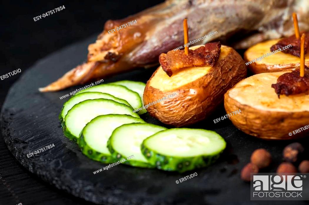 Stock Photo: potato wedges, peas pepper and leg of lamb on black plate closeup.