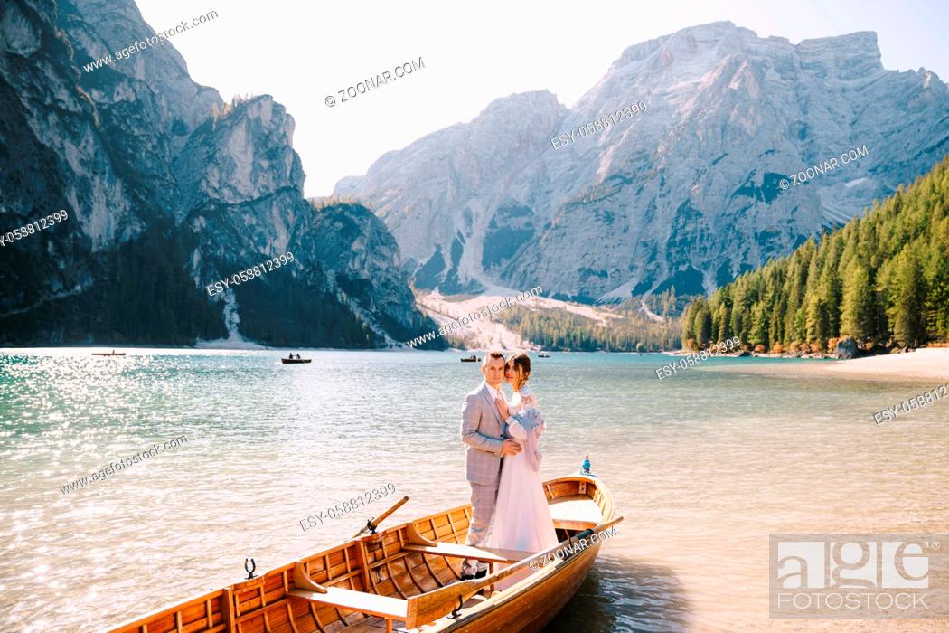 Stock Photo: Bride and groom sailing in wooden boat, with oars at Lago di Braies lake in Italy. Wedding in Europe - Newlyweds are standing embracing in boat.