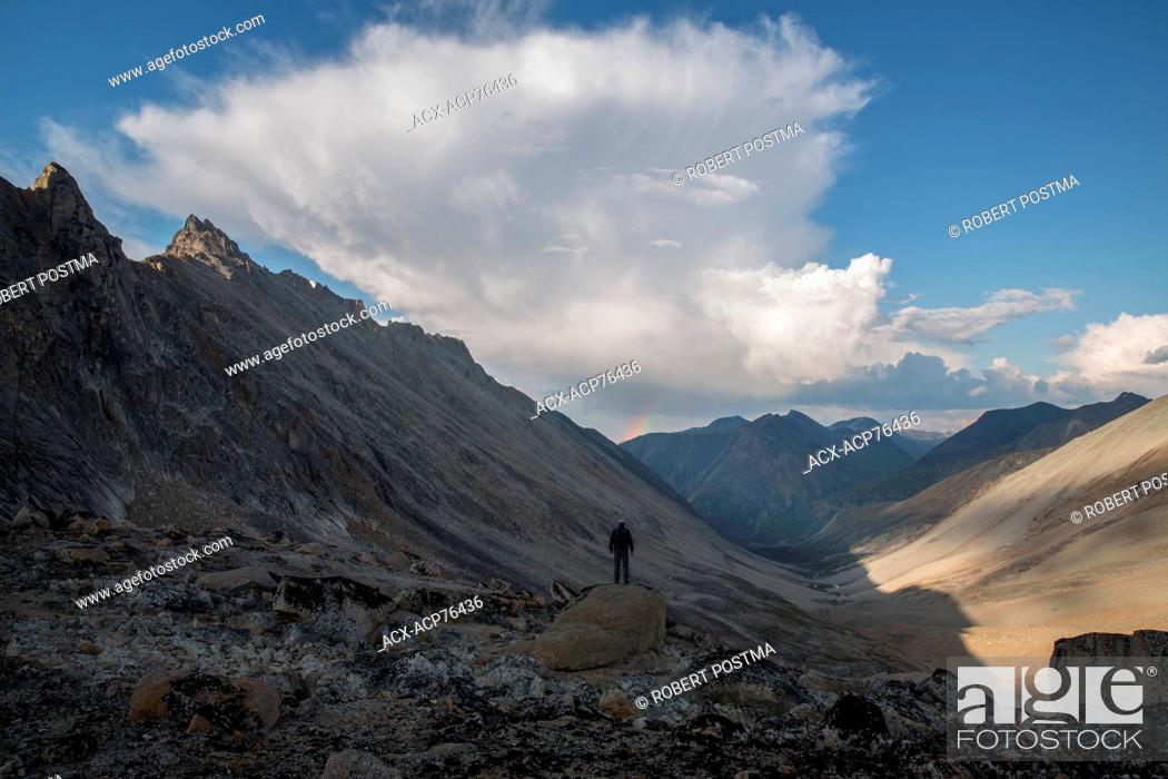 Stock Photo: Man standing on rock looking down Jones Pass in the Yukon Coast Mountains near Carcross, yukon. Storm clouds build over the mounatins towards Whtehorse.
