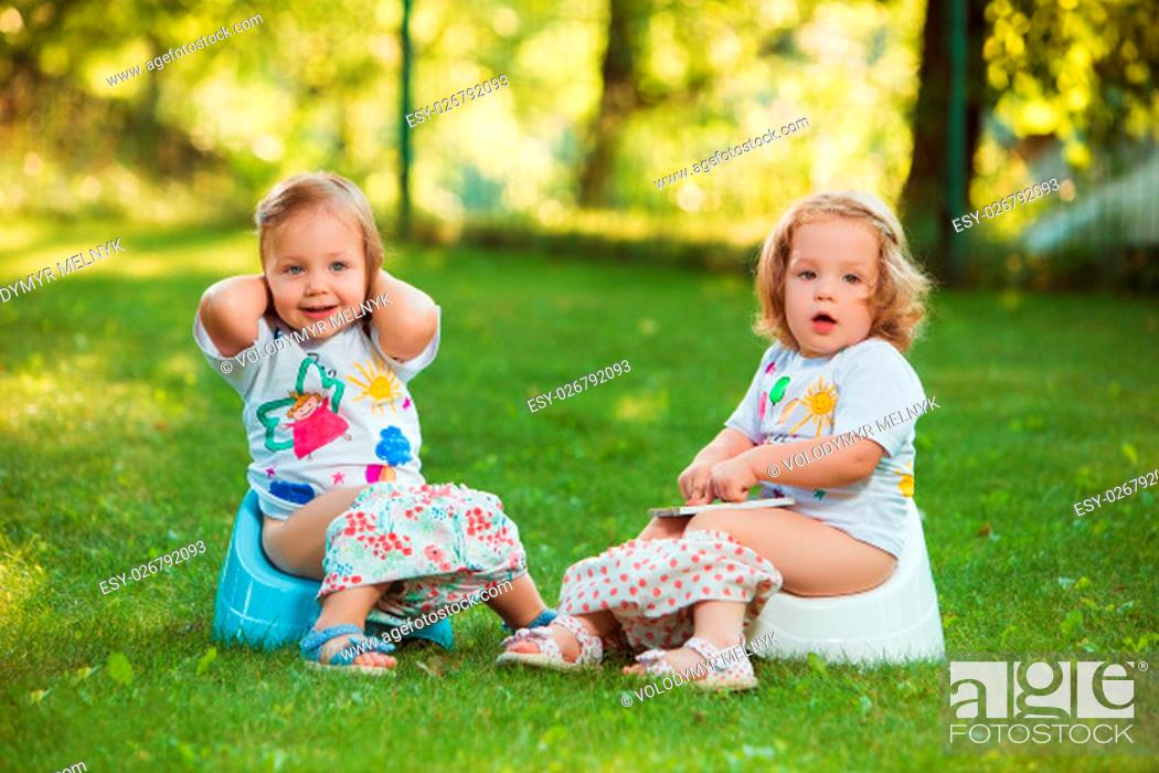 Photo de stock: The two little baby girls two-year old sitting on pots against green grass.