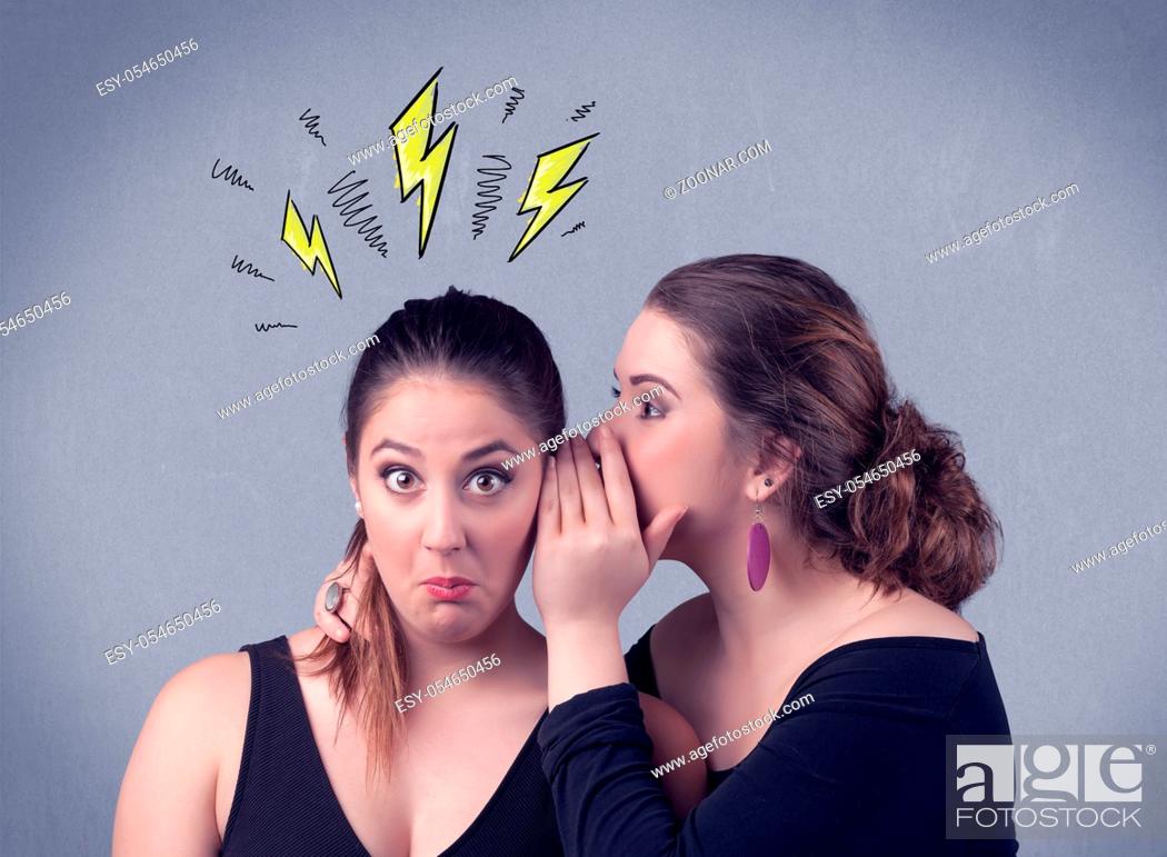 Stock Photo: A beautiful girl in black dress sharing secrets to her girlfriend concept with drawn energetic electric yellow signs above her head on the wall background.