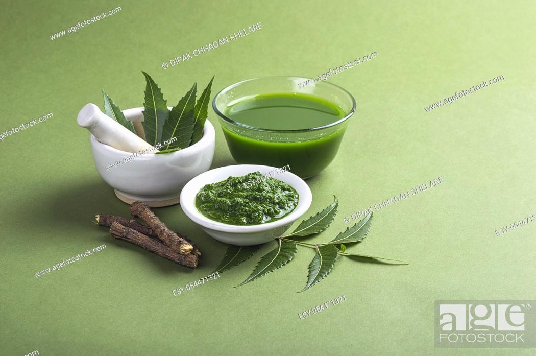 Stock Photo: Medicinal Neem leaves in mortar and pestle with neem paste, juice and twigs on green background.
