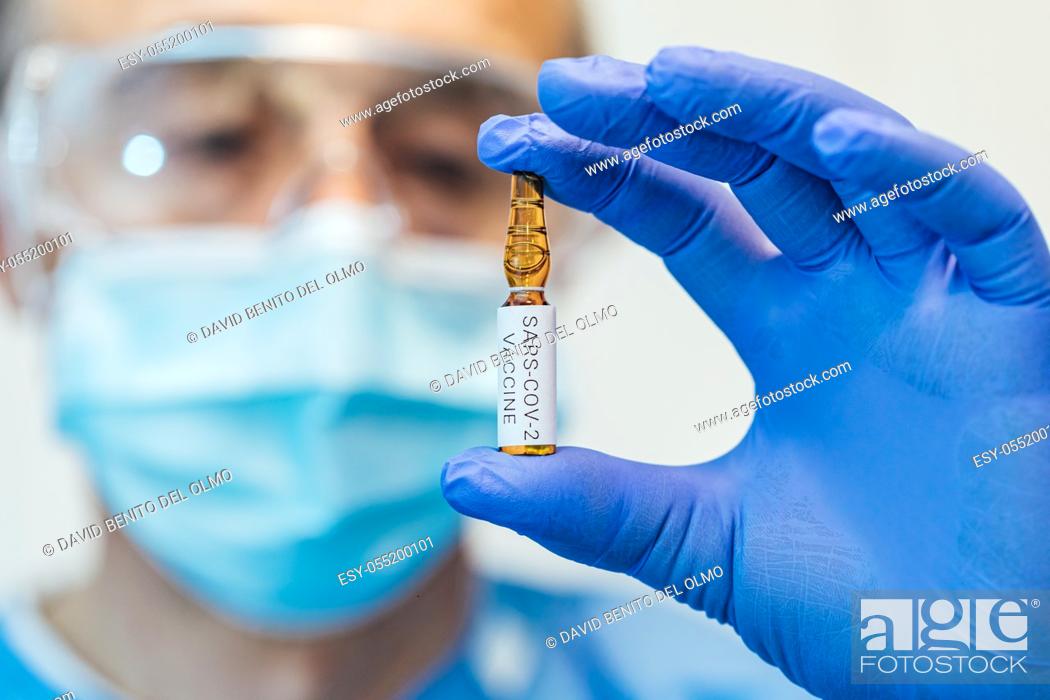 Stock Photo: Doctor's and biologist hand with blue glove holding container with COVID-19 vaccine.