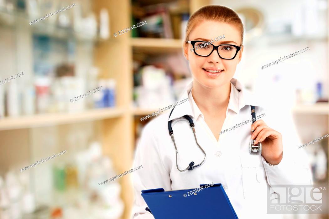 Stock Photo: Young pretty female doctor in white uniform on blurry medicine cabinet and store medicine and pharmacy drugstore for background.