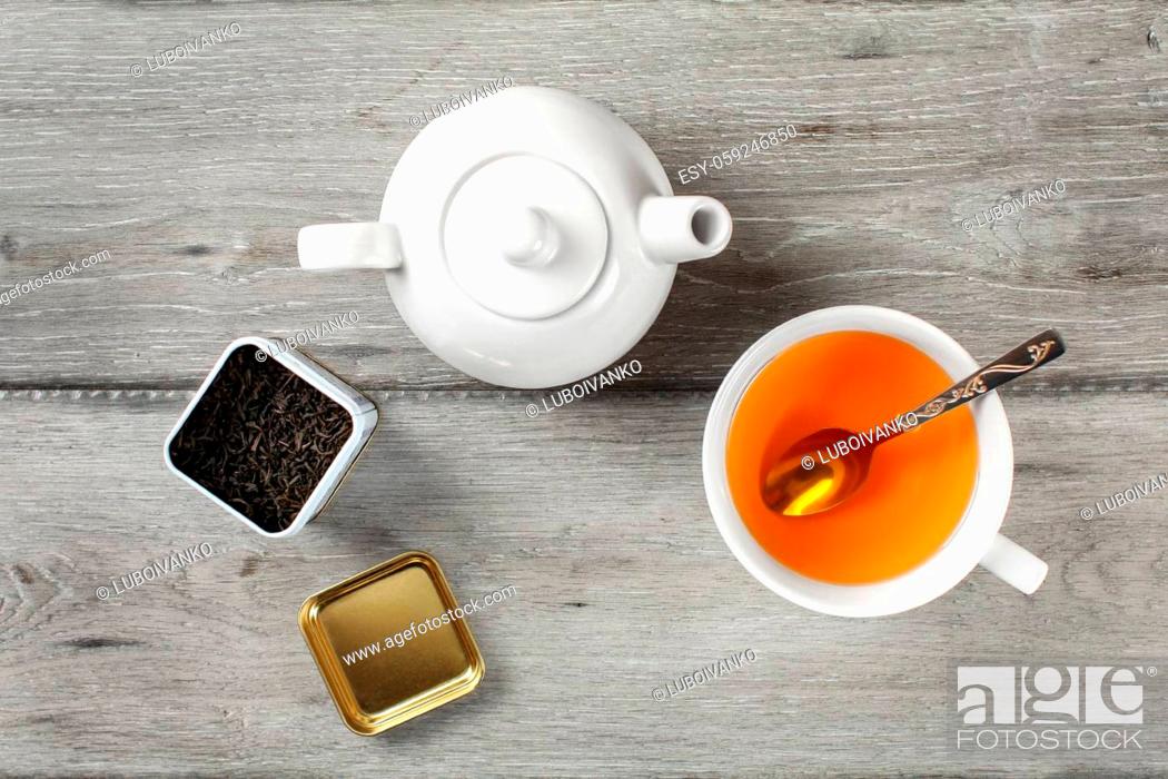 Stock Photo: Table top view - brass tea caddy, white porcelain teapot and ceramic cup with silver spoon and hot amber drink, on gray wood desk.