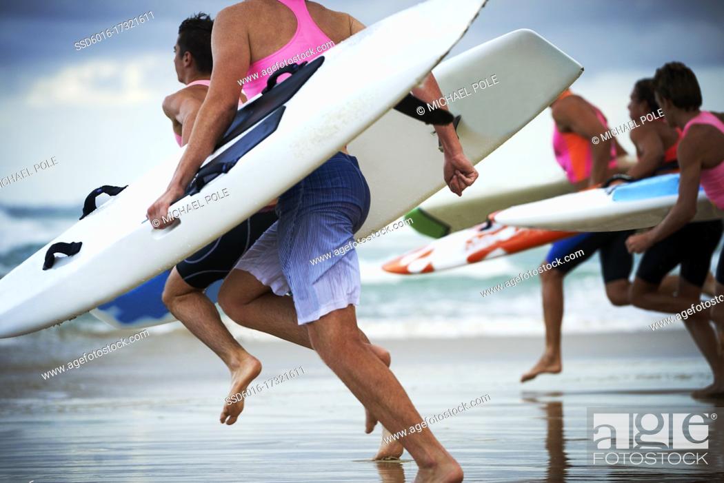 Stock Photo: Close up of team of male surf lifeguards training and running into sea holding ocean surf skis.