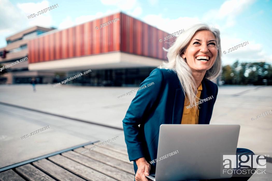Photo de stock: Cheerful businesswoman with laptop sitting at office park.
