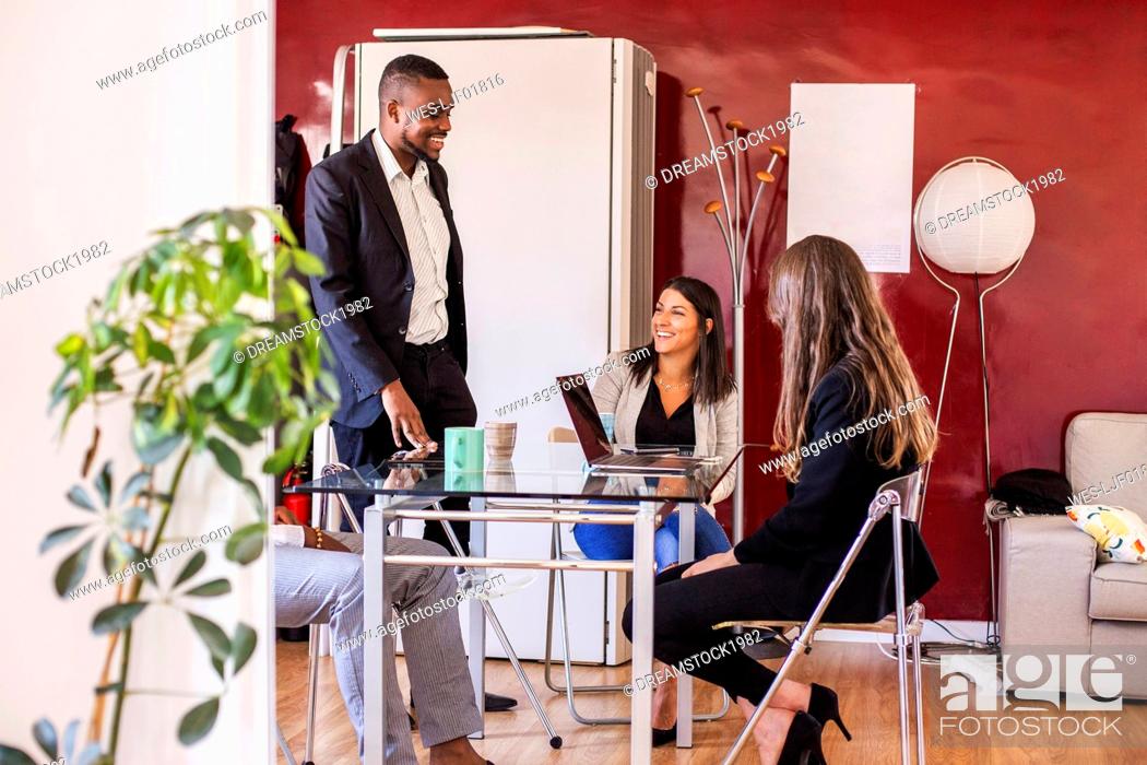 Stock Photo: Smiling businessman discussing with colleagues in coworking office.