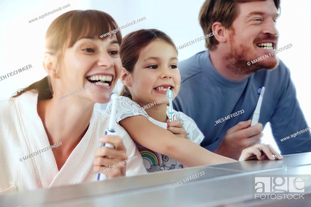 Stock Photo: Family of three brushing their teeth in front of big mirror.