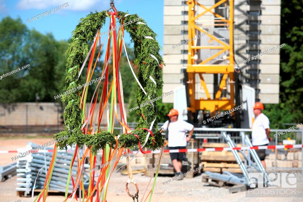 Stock Photo: 23 July 2020, Saxony-Anhalt, Wernigerode: A topping-out crown hangs in front of the shell of the new HSB locomotive workshop.