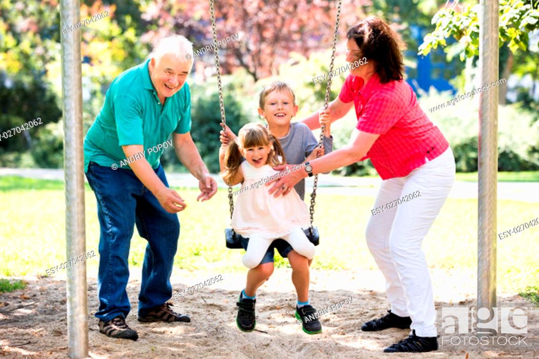 Stock Photo: Senior Grandparents Having Fun With Kids On Swing In The Park.