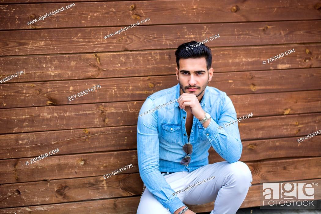 Stock Photo: Attractive young man sitting against wood wall, looking at camera.