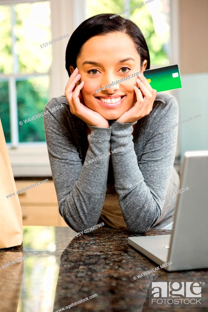 Stock Photo: Smiling brunette in kitchen holding credit card.