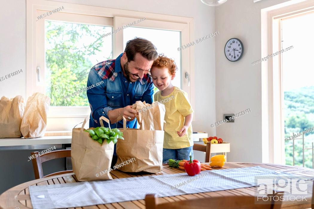 Stock Photo: Smiling man showing groceries to son in kitchen at home.
