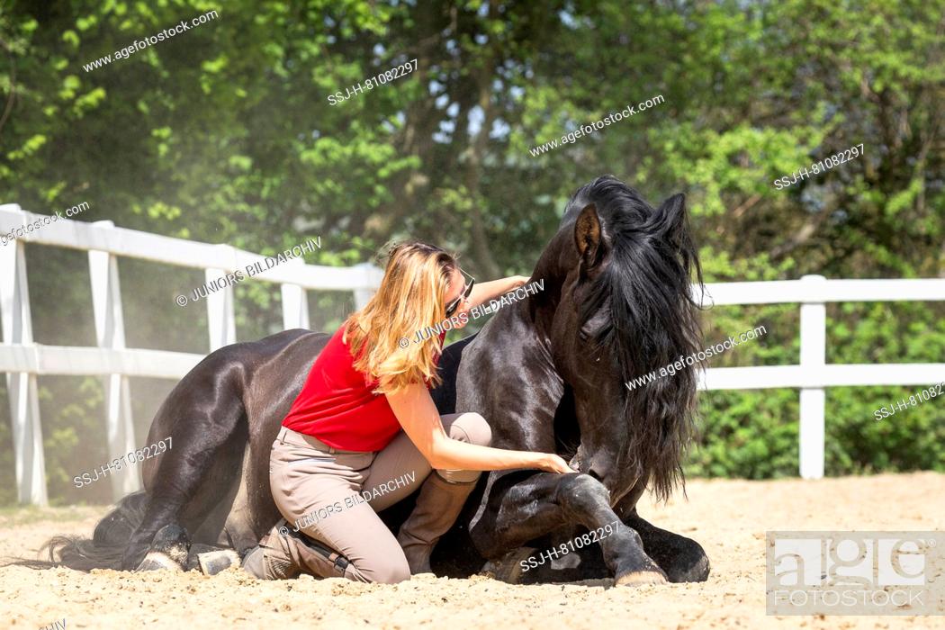 Imagen: Pure Spanish Horse, Andalusian. Woman smooching with black stallion, lying on a riding place. Germany.